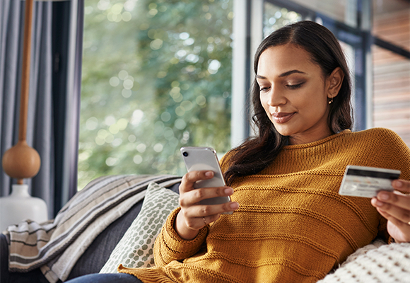 Chica sentada en su sofá con su móvil en las manos utilizando Norton Seguridad Claro Chica sentada en su sofá con su móvil en las manos utilizando Norton Seguridad Claro